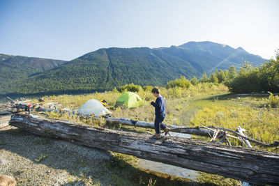 Young boy balancing on fallen log near wilderness campsite, canada.