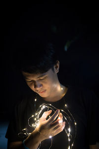 Young man holding illuminated string light at night