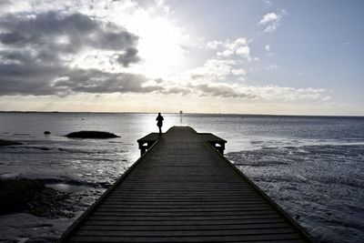 Rear view of woman by sea on pier during sunset