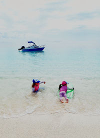 Siblings playing at beach against sky