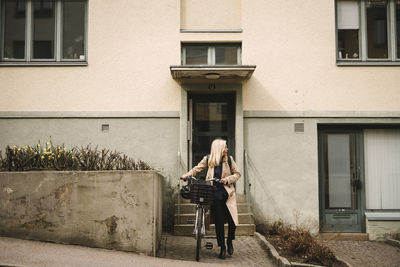 Businesswoman looking away while walking with bicycle against building