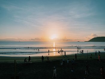 Group of people on beach against sky during sunset