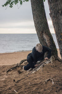 Man on tree trunk by sea against sky