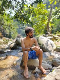 Full length of shirtless man sitting on rock