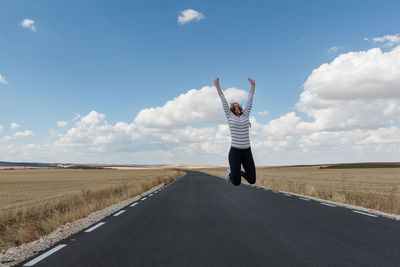 Woman jumping on road against sky