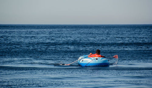 Rear view of man rowing inflatable raft in sea against clear sky