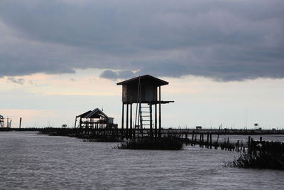 Lifeguard hut on pier by sea against sky during sunset