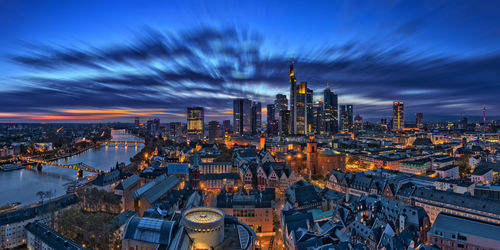 High angle view of buildings in illuminated city against cloudy sky at night