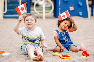 Portrait of boy and girl holding flags while playing with toys on sand