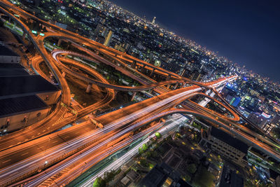 High angle view of light trails on elevated road in illuminated city at night