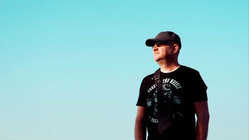 Young man wearing sunglasses standing against blue sky