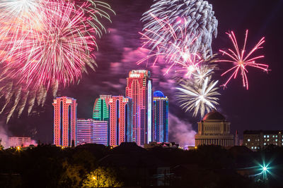 Firework display in city against sky at night