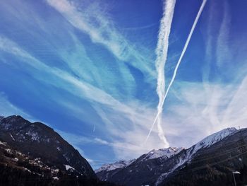 Low angle view of vapor trails in sky over rocky mountains