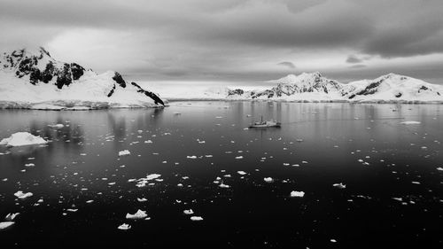 Black and white photo of sea with icebergs and ship against snowcapped mountains in antarctica
