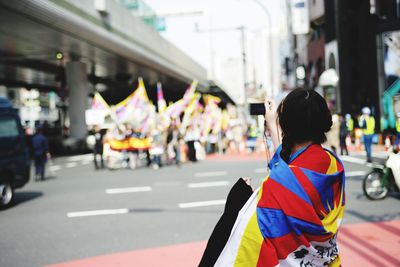 Woman wrapped in flag standing on street in city