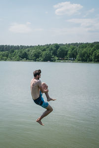 Full length of shirtless man in lake against sky