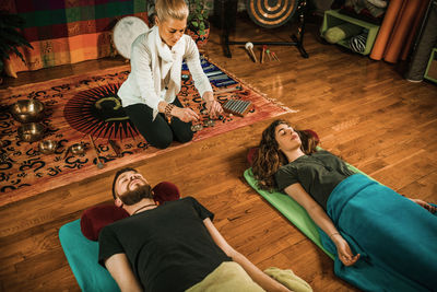 Therapist holding bells by young couple while performing music therapy at spa