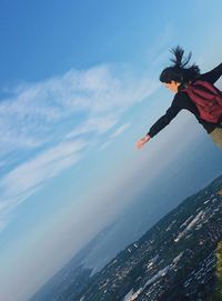 Woman with arms outstretched standing against blue sky