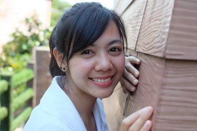 Portrait of smiling young woman standing by wooden wall