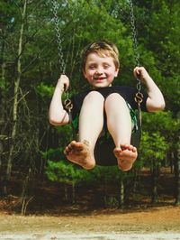 Full length of playful boy swinging in playground