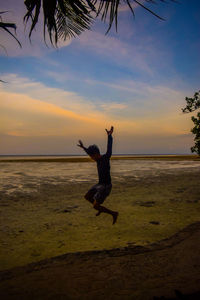 Man jumping on beach against sky during sunset