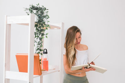 Young woman standing by potted plant at home