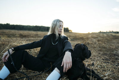 Portrait of young woman sitting on field against sky