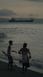 Rear view of people on beach against sky during sunset