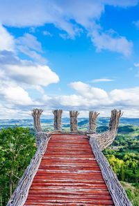 Wooden walkway amidst plants and trees against sky