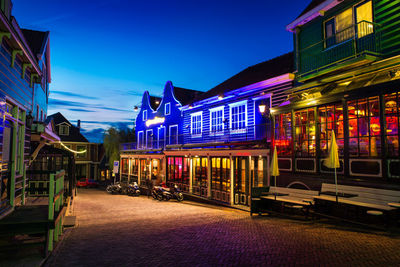 Illuminated street amidst buildings against sky at night