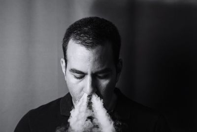 Close-up of man emitting smoke from nose against wall