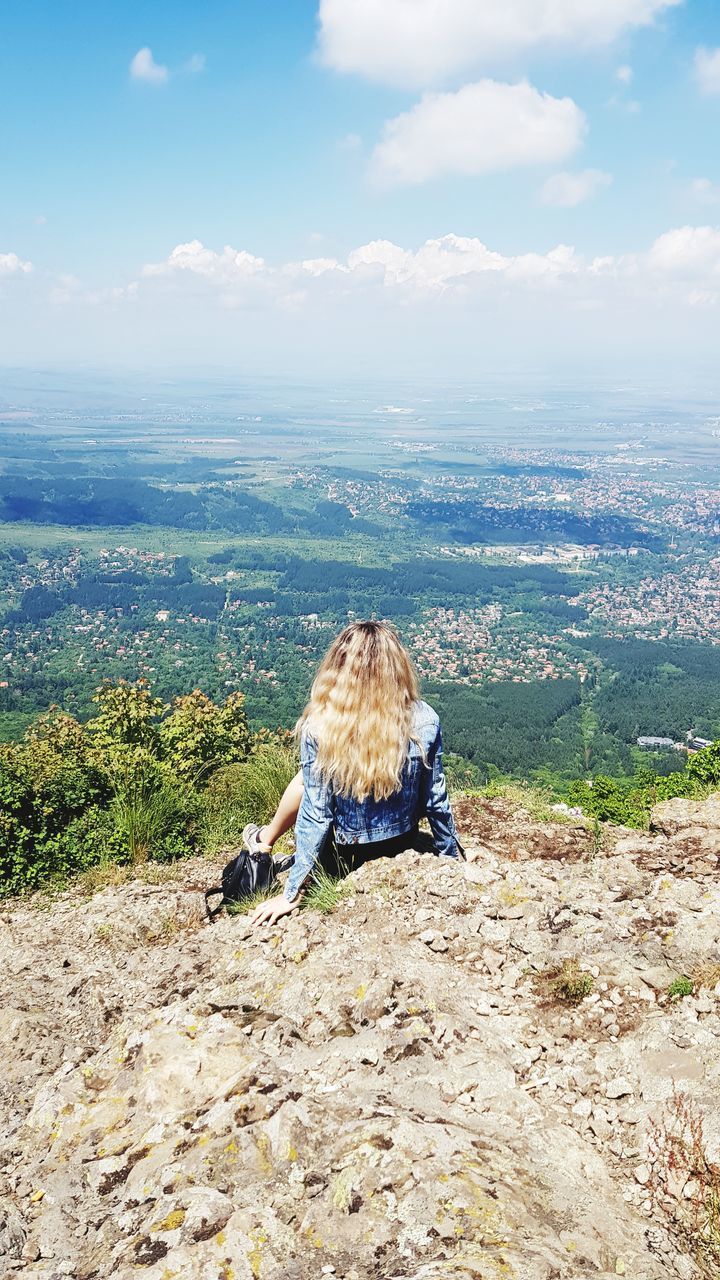 REAR VIEW OF MAN SITTING ON ROCK