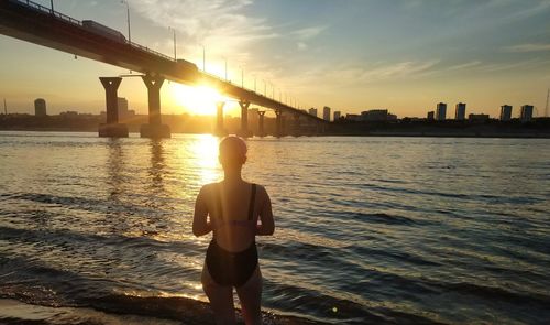 Rear view of woman standing at beach against sky during sunset