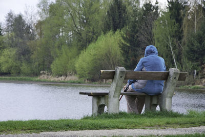 Rear view of man sitting on bench by lake