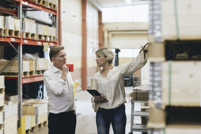 Female manger explaining senior businessman in factory warehouse