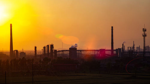 Smoke emitting from factory against sky during sunset