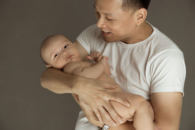 Close-up of father holding baby against gray background