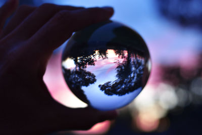 Close-up of hand holding crystal ball against sky