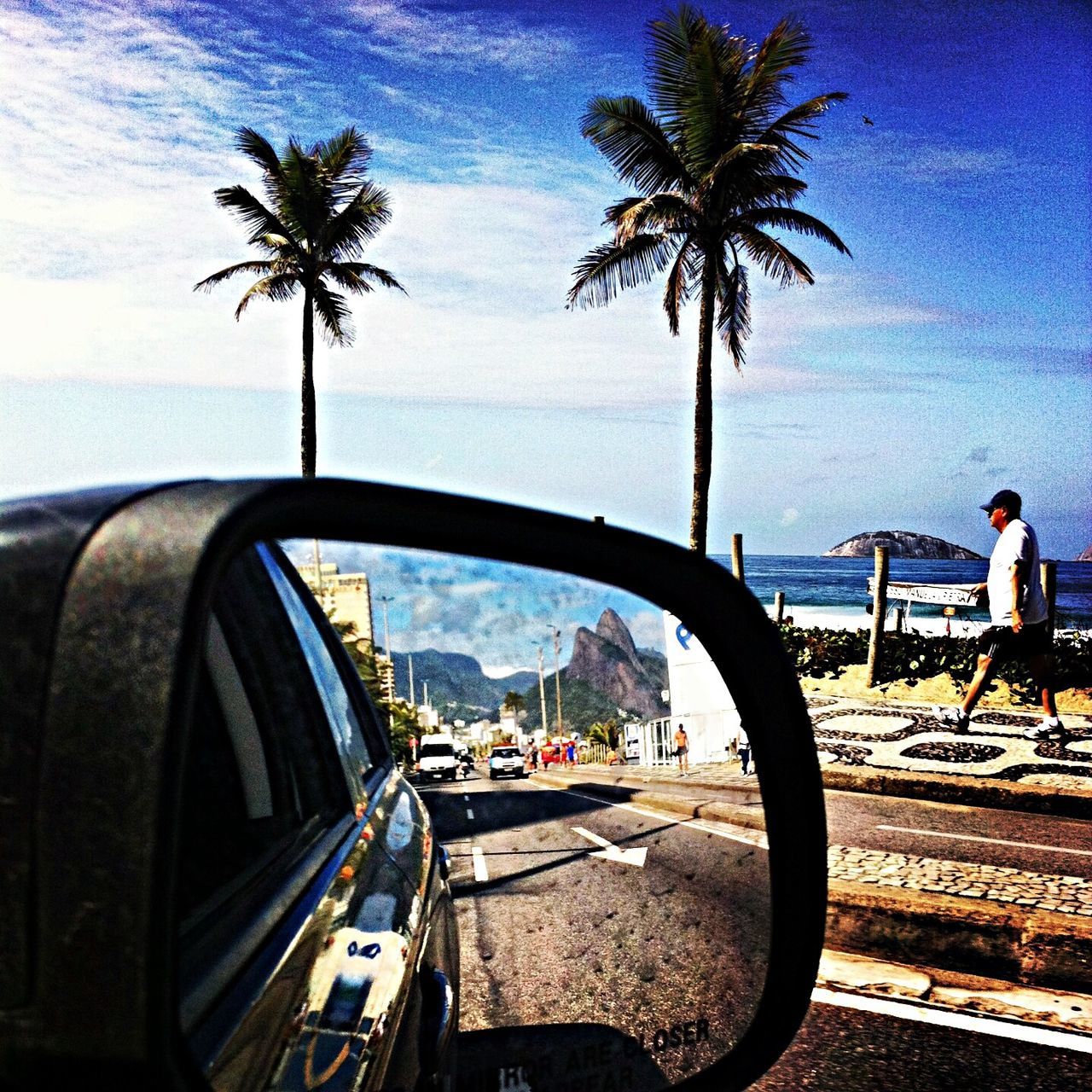 palm tree, transportation, tree, sea, mode of transport, water, sky, land vehicle, beach, horizon over water, car, travel, nautical vessel, cloud - sky, shore, nature, boat, road, tree trunk, incidental people