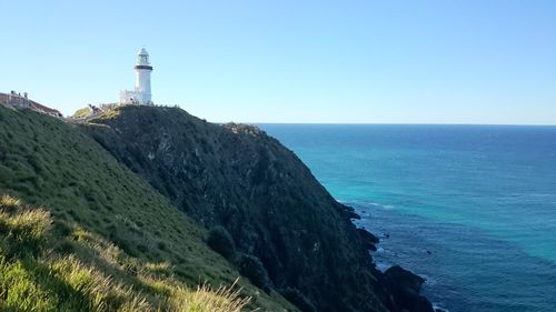 Lighthouse amidst sea and buildings against clear sky