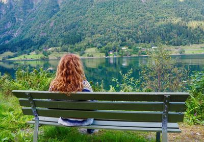 Woman sitting on grass by lake against trees