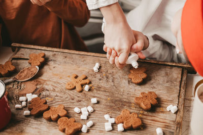 Children decorate the christmas gingerbread man with white frosting on a wooden background. 