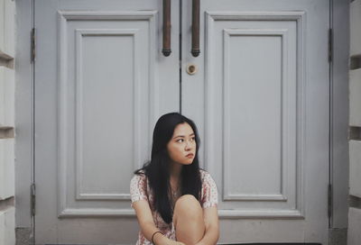 Young woman looking away while sitting against door