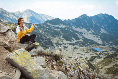 Woman sitting on rock by mountains against sky