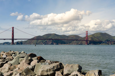 View of suspension bridge over sea against cloudy sky