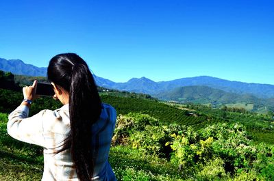 Rear view of woman photographing landscape from mobile phone