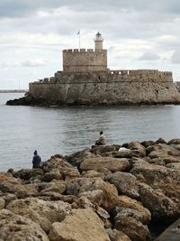 People sitting on rock by sea against sky