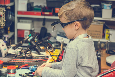 Side view of boy with work tools on table sitting in workshop