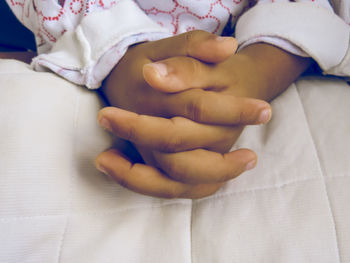 Cropped image of child with hands clasped on bed