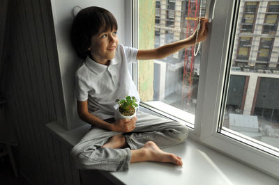 Brown haired boy sitting at windowsill and looking on street